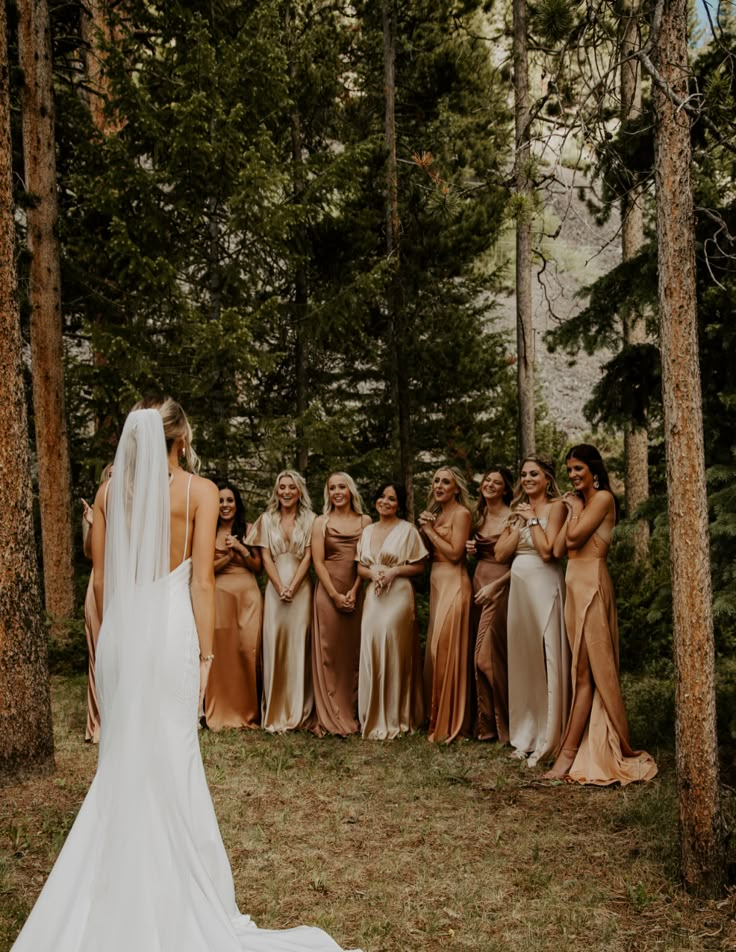 a bride and her bridal party standing in the woods with their backs to each other