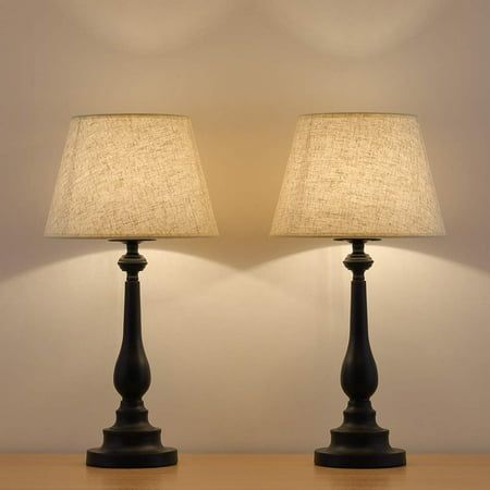 two lamps sitting on top of a wooden table next to each other with a white wall in the background