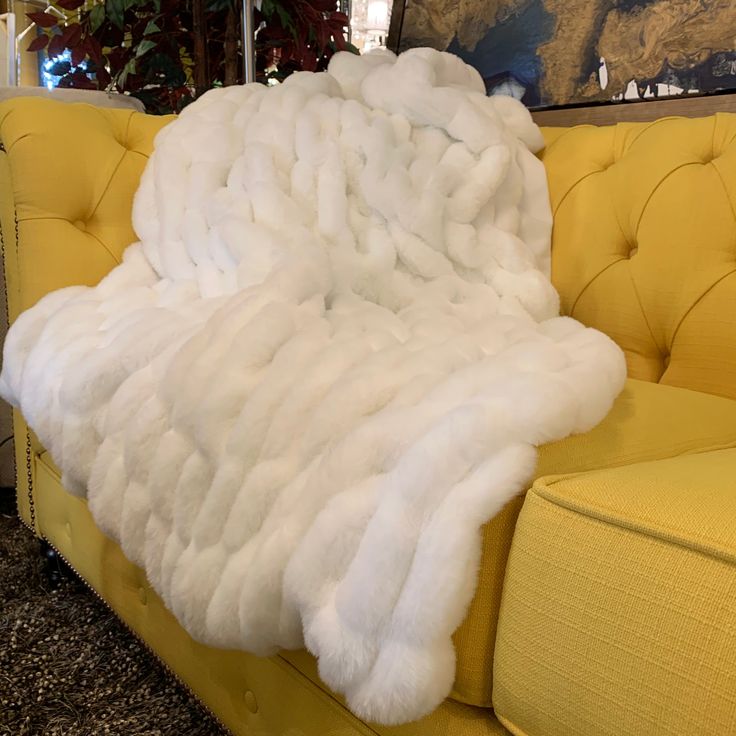 a large white fur blanket sitting on top of a yellow couch