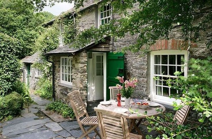 an outdoor table and chairs in front of a stone building with green doors on the outside