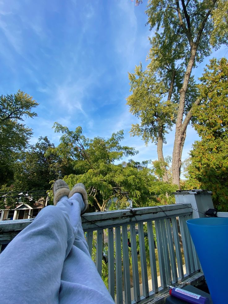 someone is sitting on a bench with their feet up in the air and trees behind them