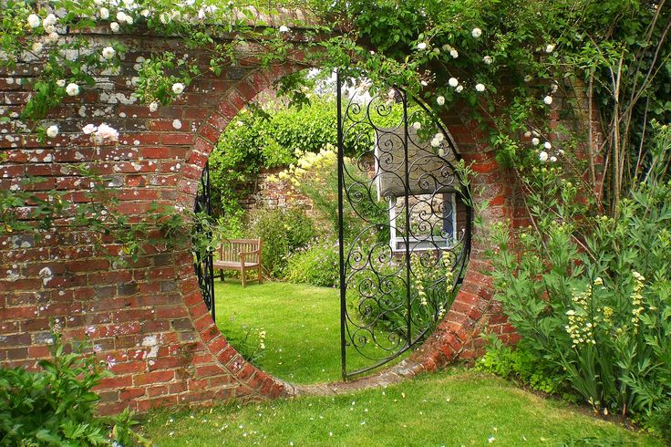 an iron gate in the middle of a garden with white flowers growing on it and green grass