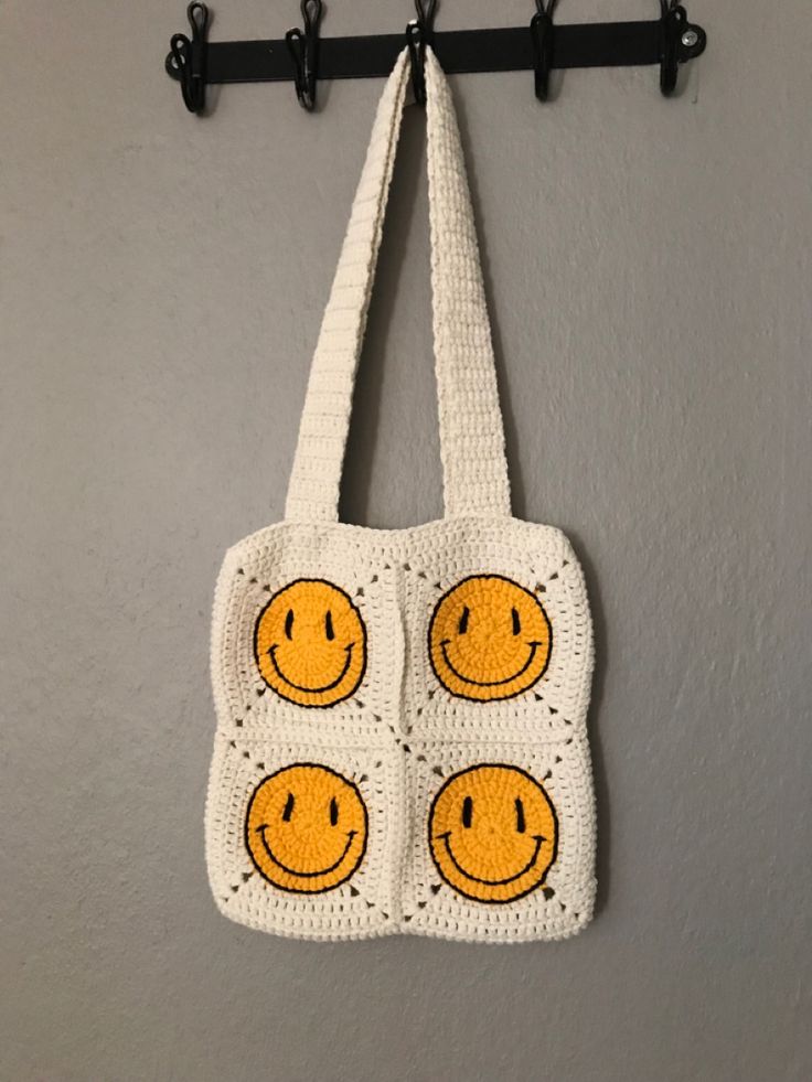 a crocheted smiley face bag hanging from a hook on a wall with hooks