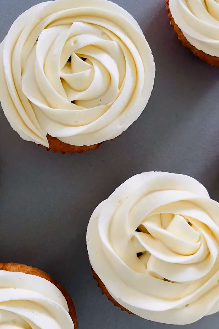 four cupcakes with white frosting on a gray surface, one is cut in half