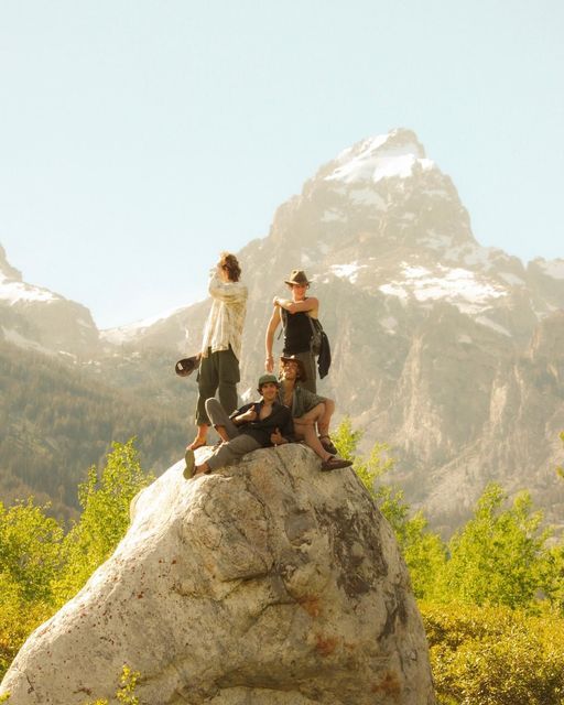 three people standing on top of a large rock in the middle of a mountain range