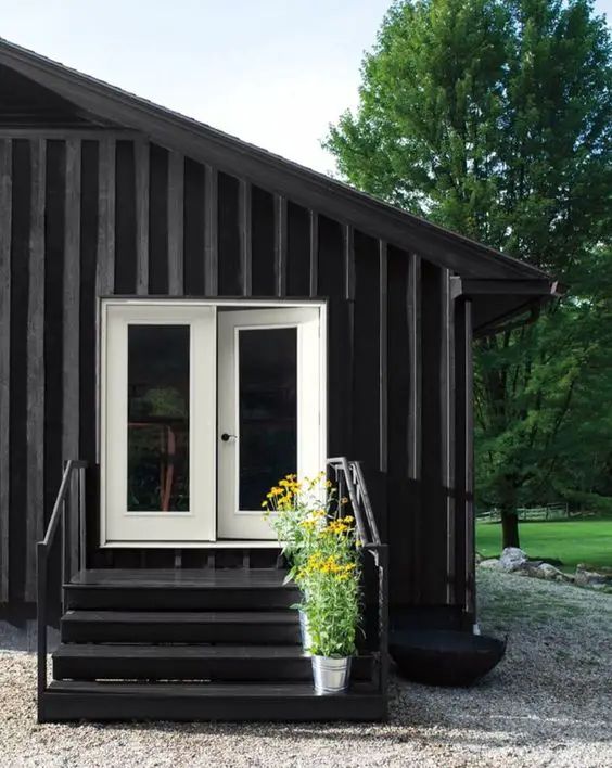 there is a small black house with white doors and steps leading to the front door