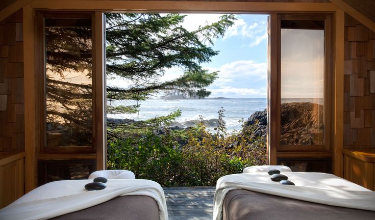 two massage beds sitting in front of an open window overlooking the ocean and trees on either side