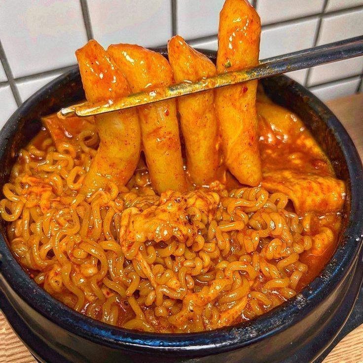 a bowl filled with noodles and meat on top of a wooden table next to a tiled wall