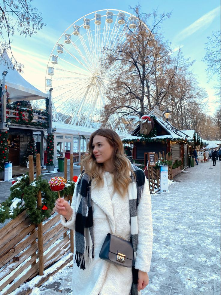 a woman standing in front of a ferris wheel and holding a christmas ornament