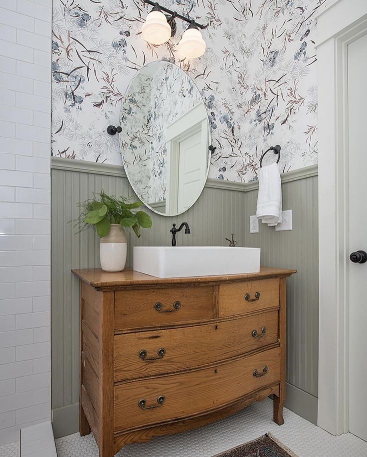 a bathroom with floral wallpaper and a wooden dresser in front of a mirror on the wall