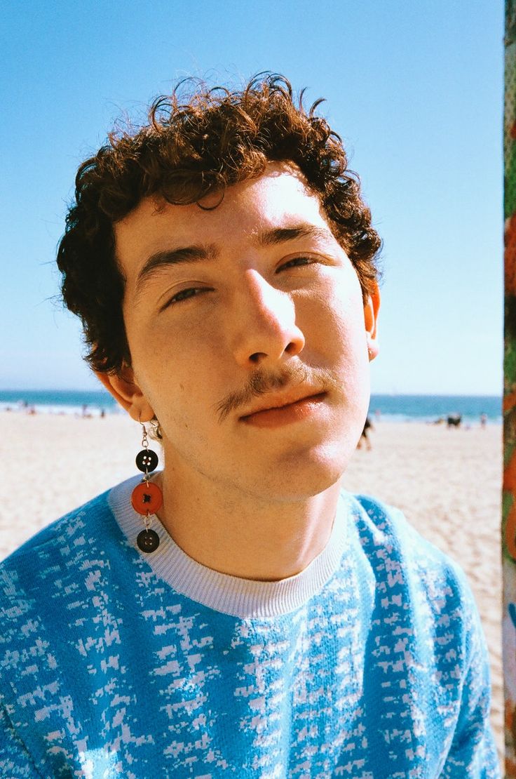 a man with curly hair wearing earrings on the beach