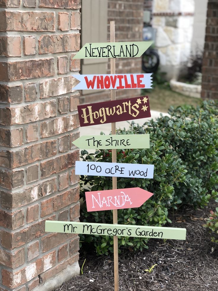 a wooden sign with many different signs on it in front of a brick wall and bushes