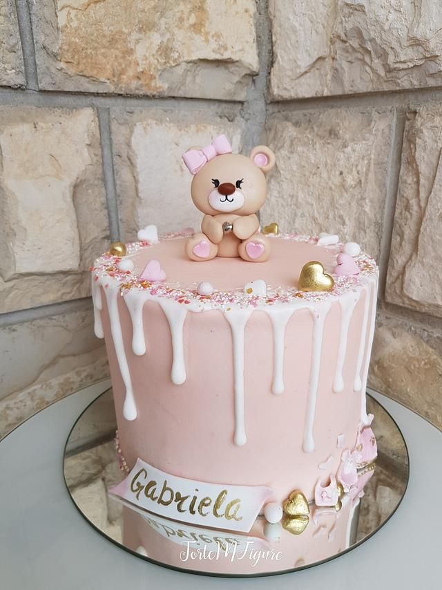 a pink cake with white icing and a teddy bear on top