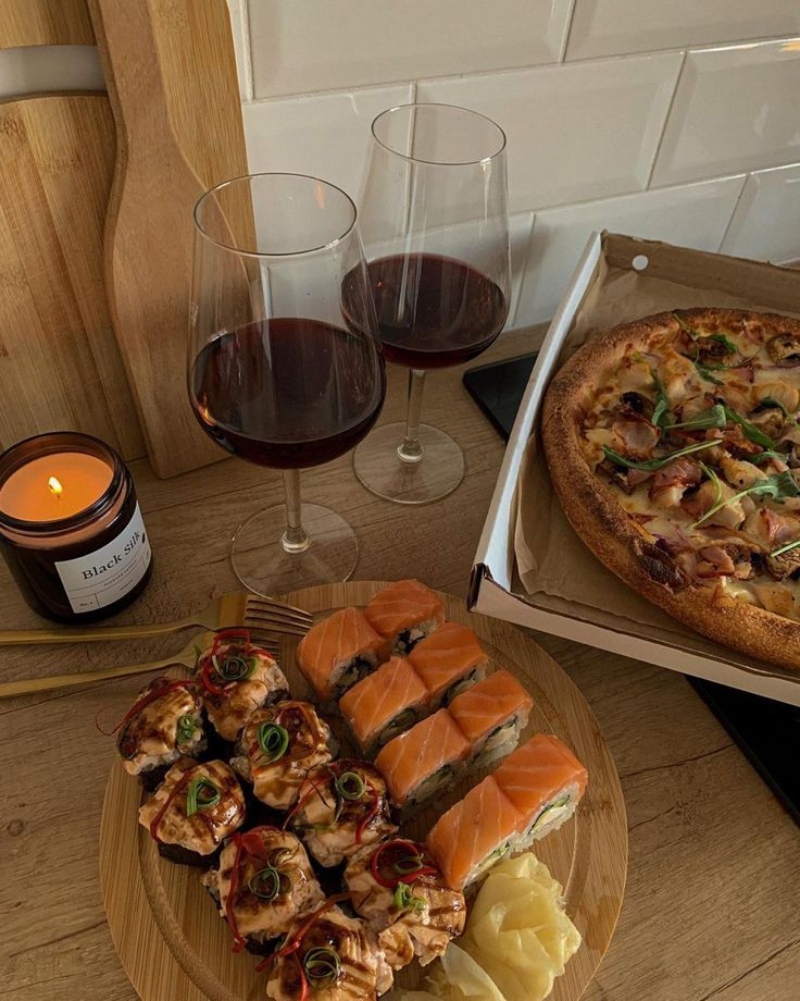 two pizzas and some appetizers are sitting on a table with wine glasses