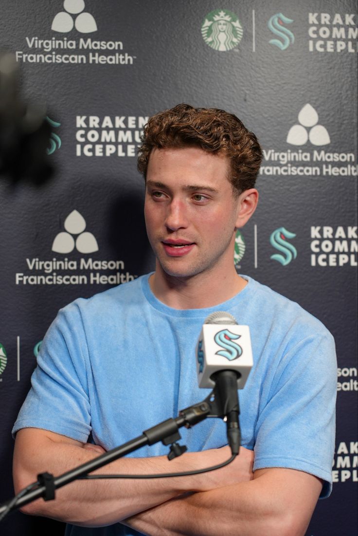 a man standing in front of a microphone with his arms crossed and looking at the camera