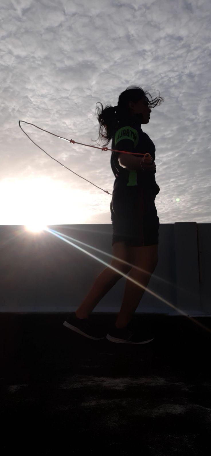 a woman flying a kite on top of a roof under a cloudy sky with the sun behind her