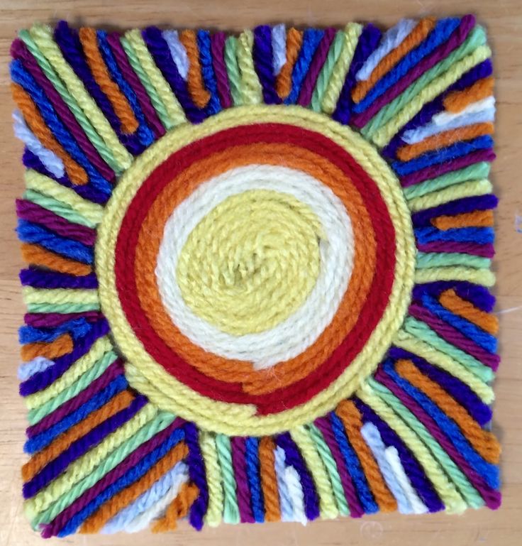 a multicolored crocheted placemat on a wooden table with yarn in the center