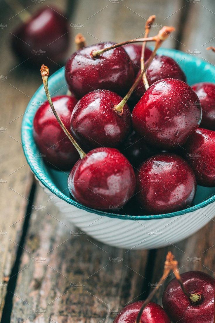 a bowl filled with cherries on top of a wooden table