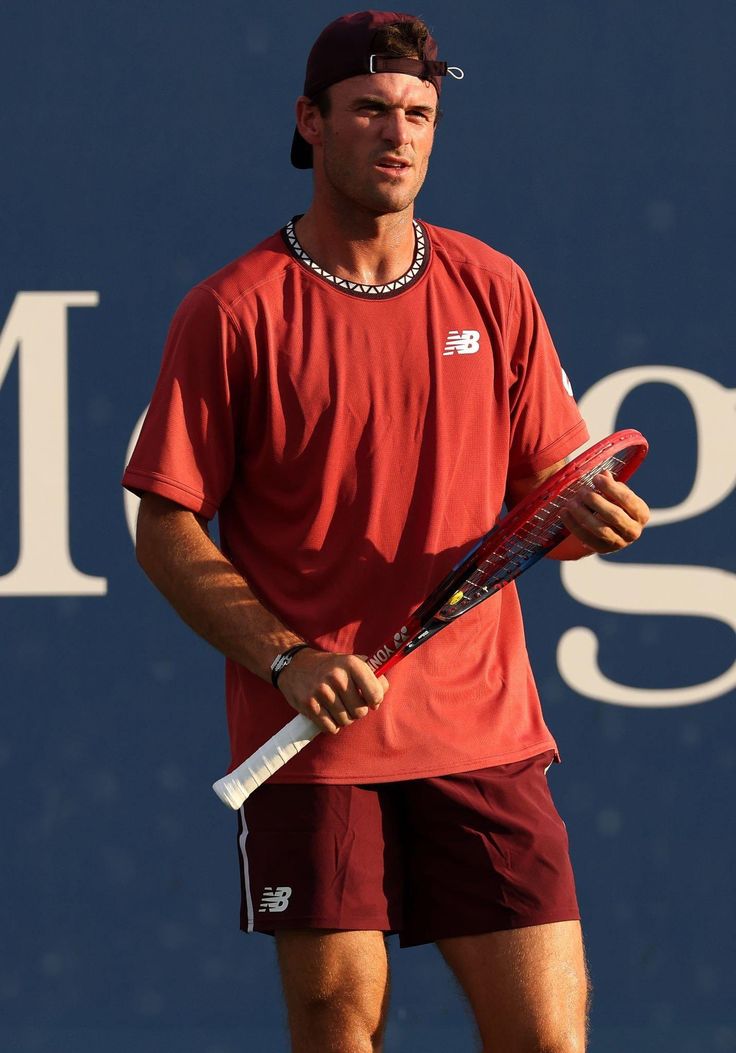 a man holding a tennis racquet on top of a tennis court with a blue wall behind him