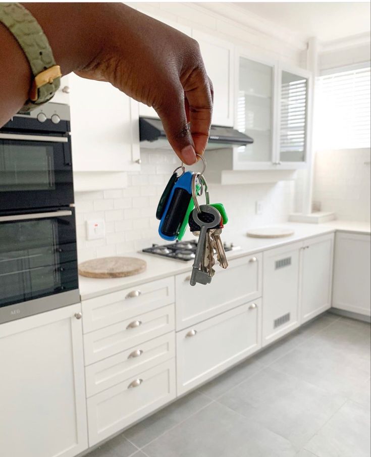 a hand holding keys in front of a kitchen with white cabinets and counter top space