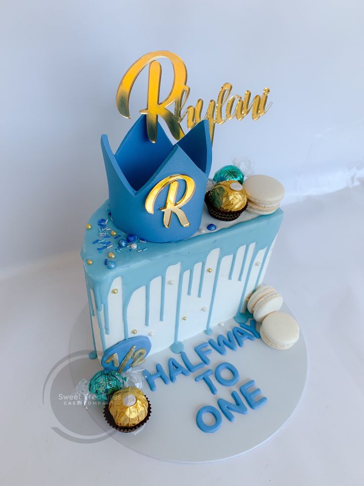 a blue cake with gold letters and decorations on it's top is sitting on a white table