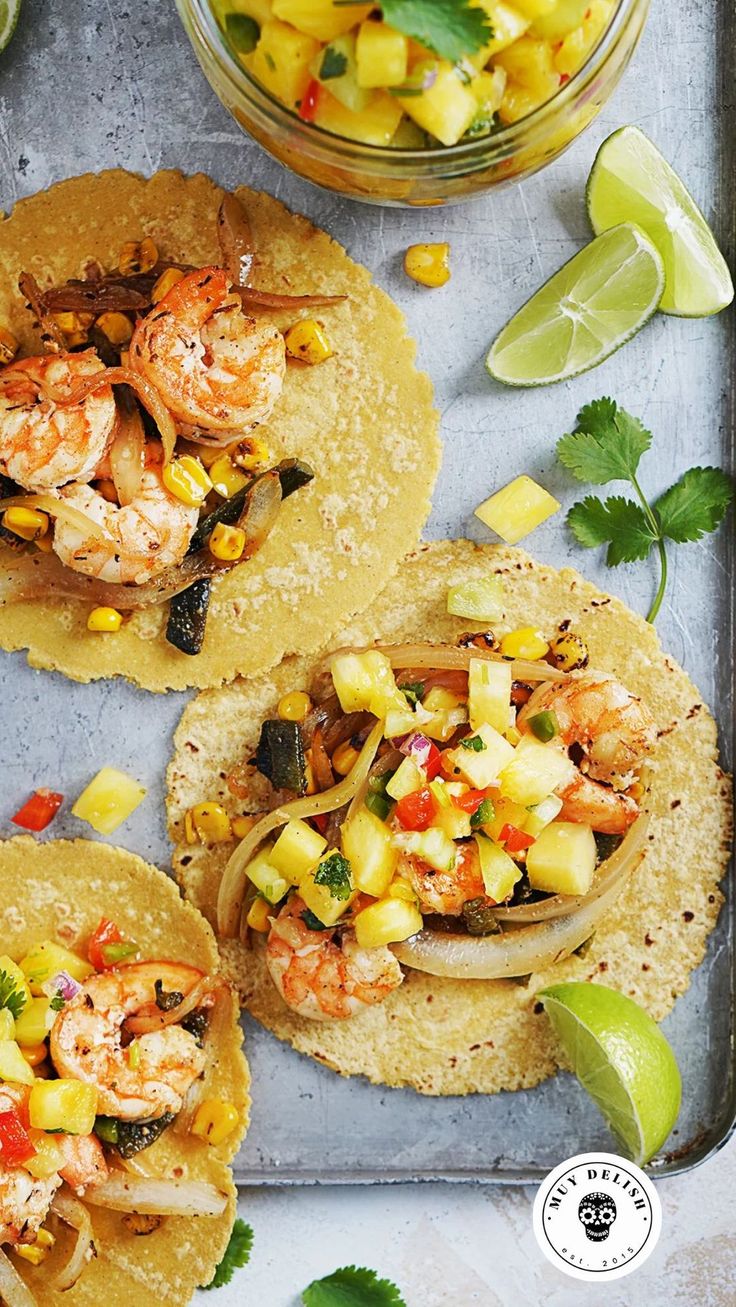 three tacos with shrimp, pineapple salsa and lime wedges on a tray