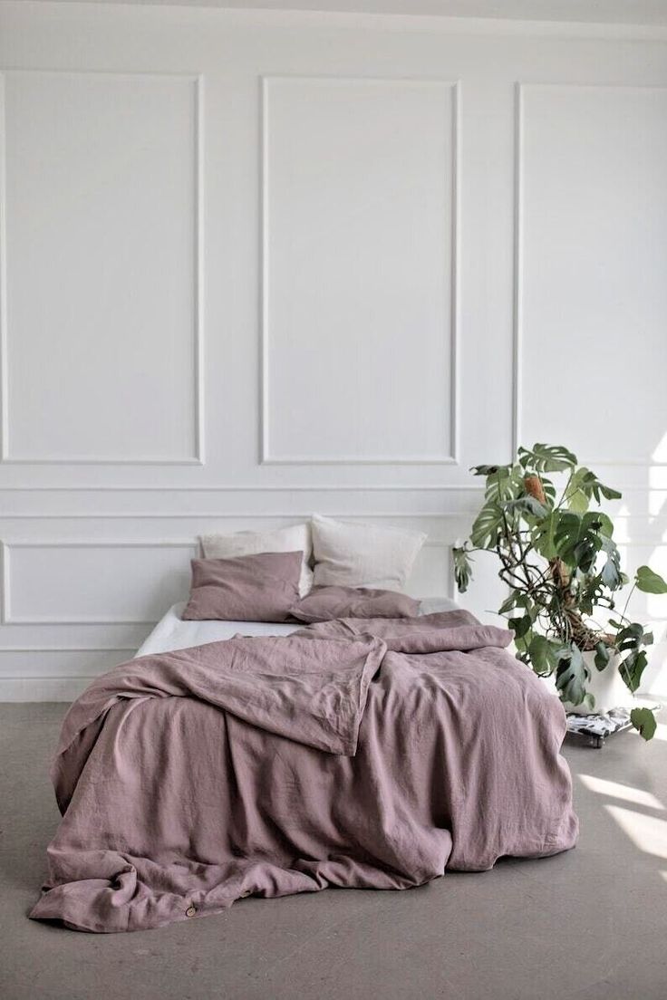 an unmade bed sitting next to a plant in a room with white paneled walls