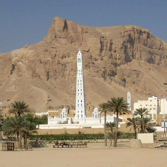 a tall white clock tower sitting in the middle of a desert area next to palm trees