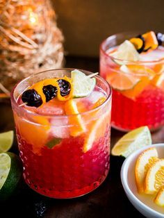 two glasses filled with fruit and garnish on top of a table