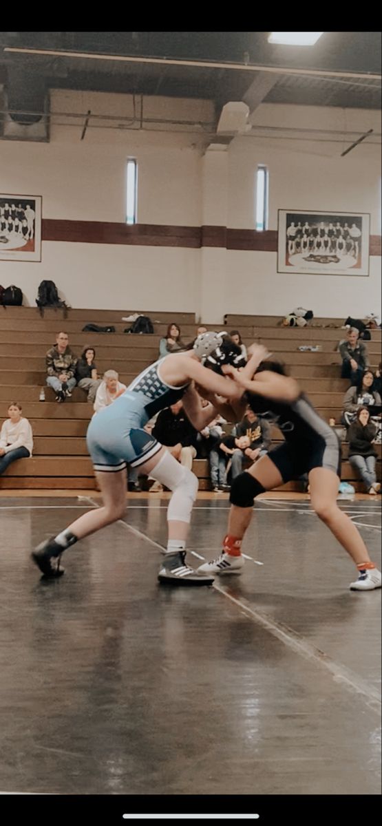 two women wrestling in a gym with people watching