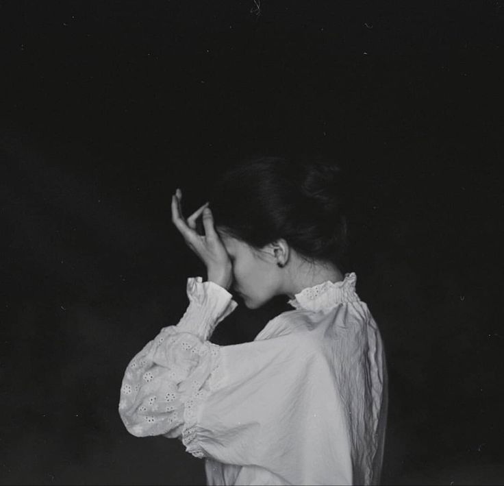 a black and white photo of a woman with her hands to her face, in the dark