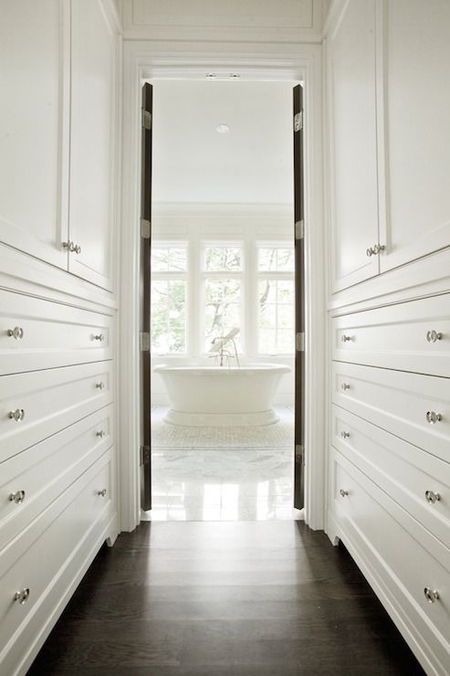 an open door leading to a bathroom with white walls and drawers on either side of the bathtub