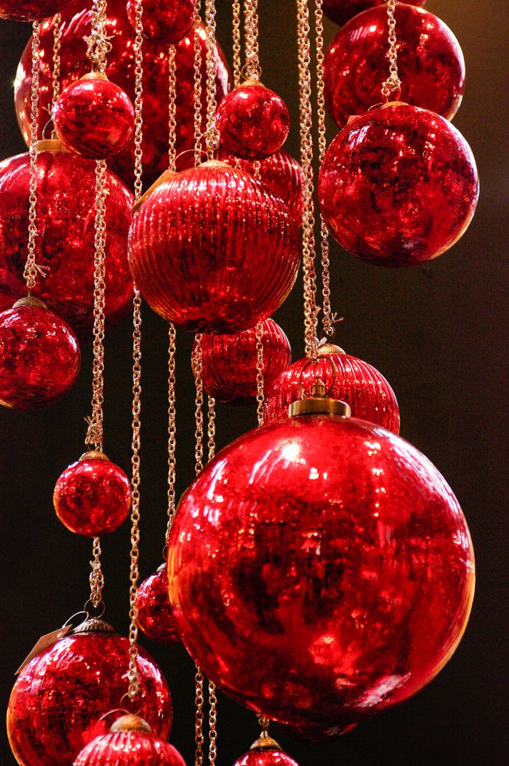 red christmas ornaments hanging from chains on a black background