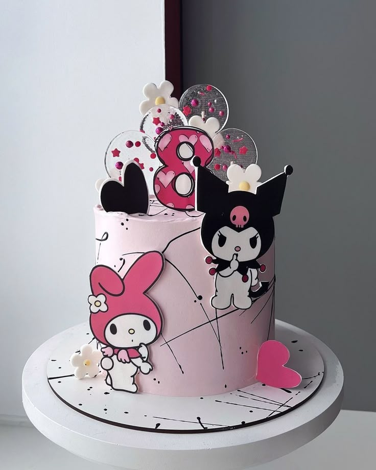 a pink and white cake with hello kitty decorations on it's top is shown