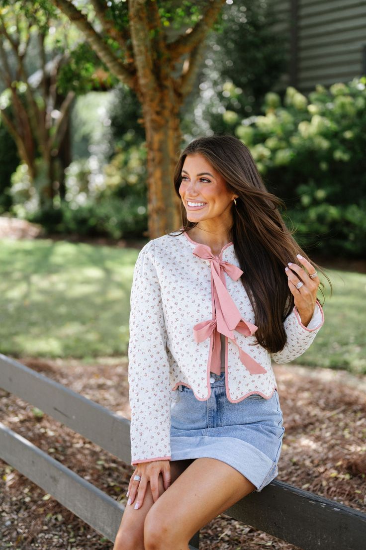 Effortlessly stylish and practical, the Floral Quilted Bow Jacket in Pink Floral is the perfect addition to your wardrobe. The ivory quilted fabric provides warmth and comfort, while the feminine pink and green floral print adds a touch of elegance. Complete with pink trim and tie closures on the front, and a scalloped cropped bottom hem, this jacket is both functional and fashionable. Upgrade your outerwear game with this must-have piece! 65% cotton, 35% linen Model is 5'6" with a 35" bust, 26" Feminine Pink Floral Print Outerwear, Spring Cream Outerwear With Floral Print, Cream Floral Print Outerwear For Spring, Fitted Beige Outerwear With Floral Print, Fitted Beige Floral Print Outerwear, Feminine Pink Spring Cardigan, Feminine Pink Cardigan For Spring, Spring Fitted Cardigan With Floral Print, Spring Floral Print Outerwear For Daywear