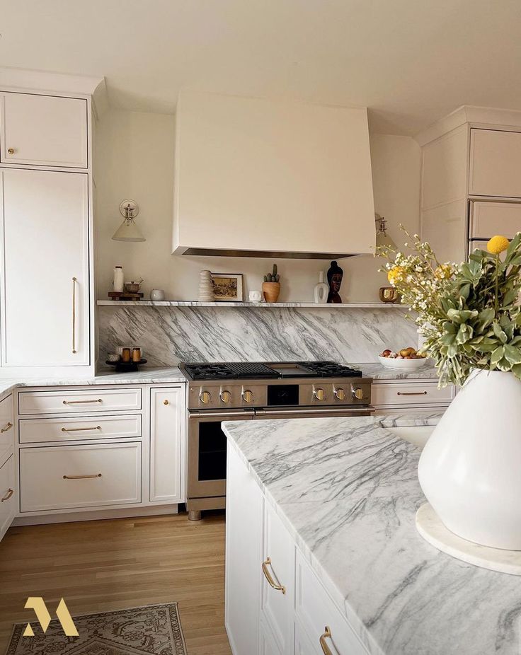 a kitchen with marble counter tops and white cabinets, yellow flowers in a vase on the island