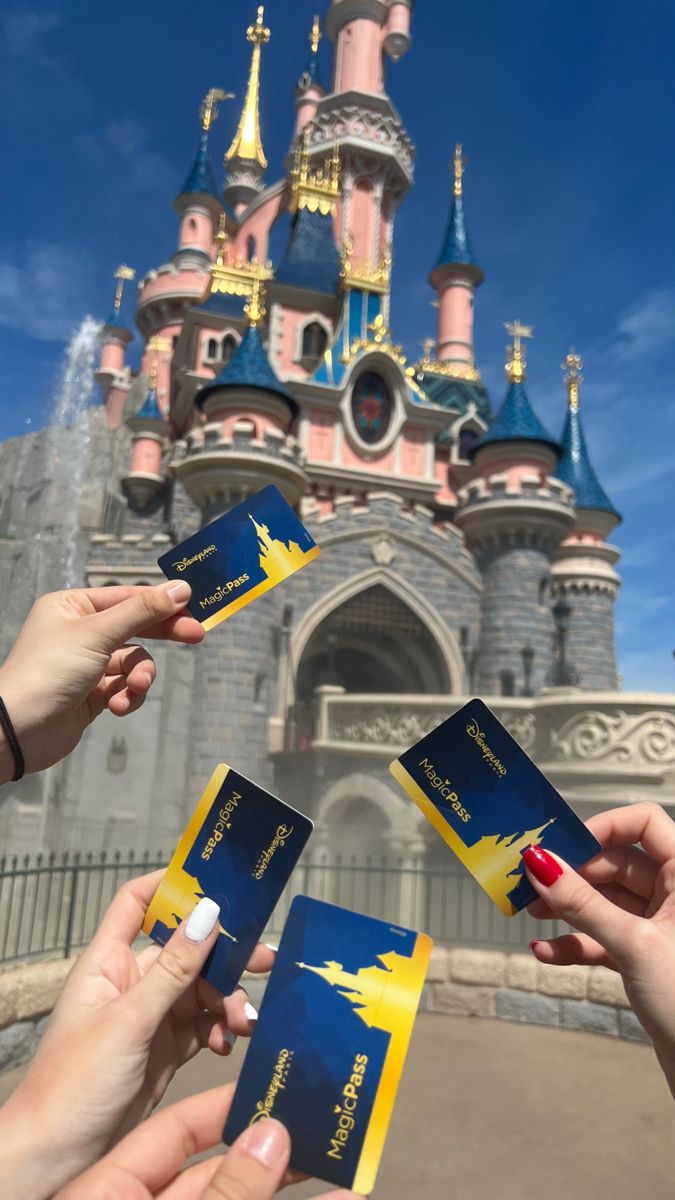 three people holding up their passport in front of a castle with the disney world logo on it