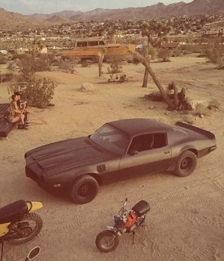 a black car parked in the middle of a dirt field next to a motorbike