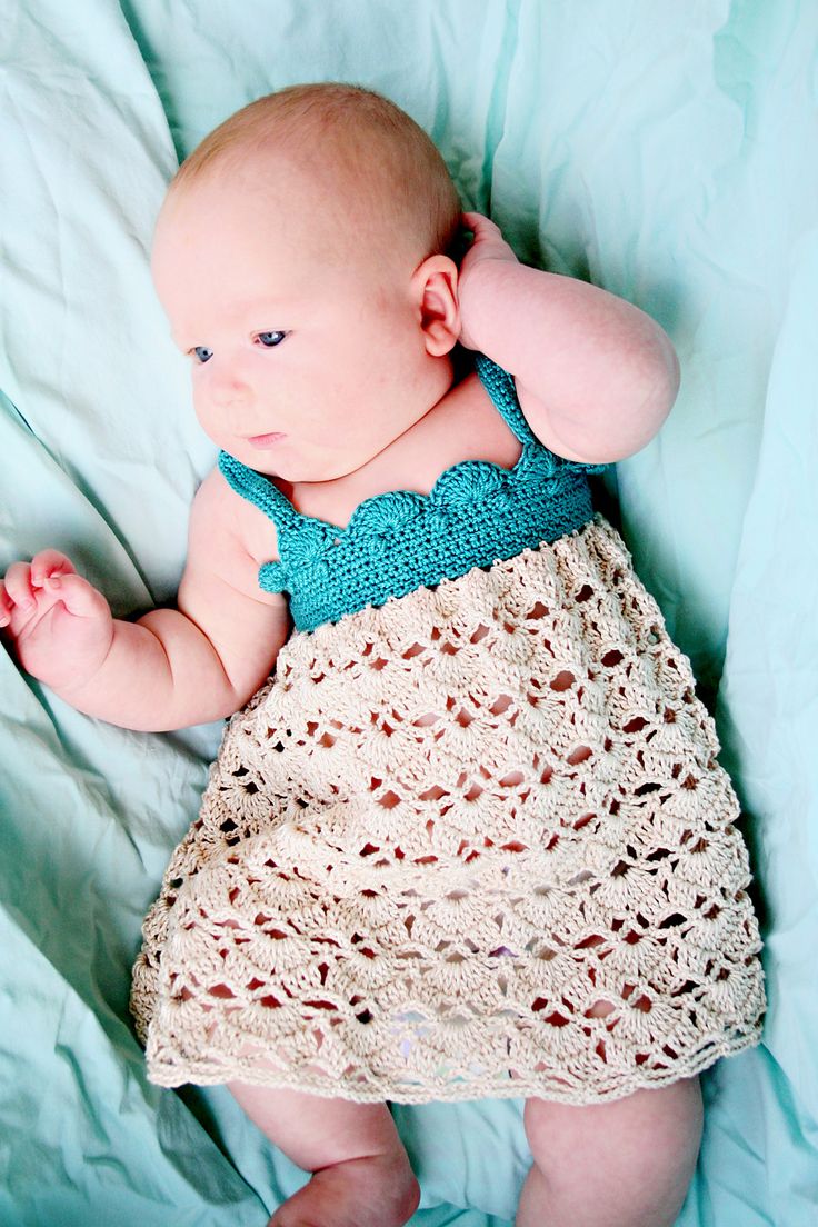 a baby laying on top of a bed wearing a crochet dress and looking at the camera