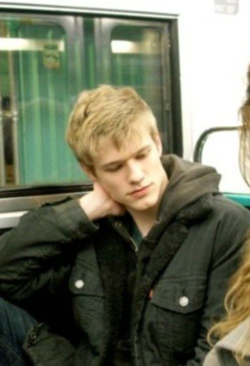 a young man sitting on a subway train next to a woman who is holding her head