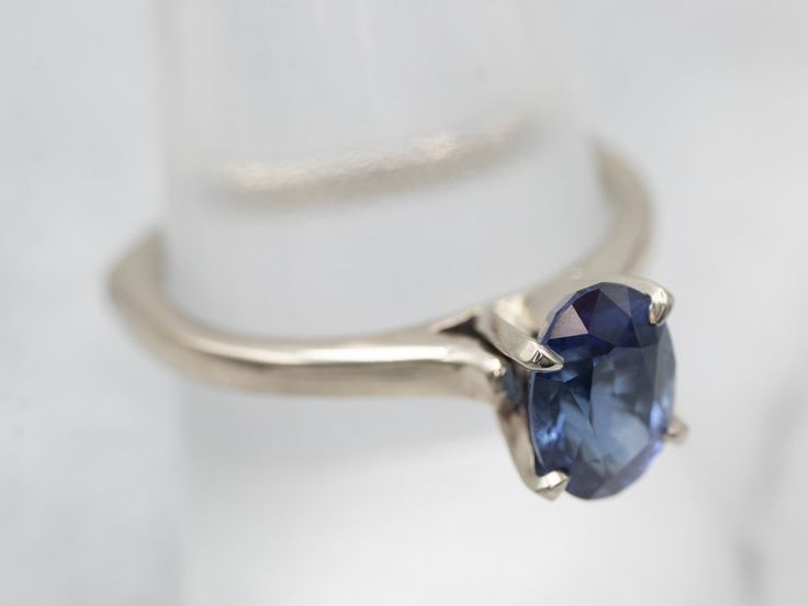 This is a well-proportioned ring, classic and sophisticated. The brightly polished sides have a great heft to them, and this is comfortable on the finger, with a rich feel. We've set the center with a bright blue Ceylon sapphire that has glittering navy and cobalt highlights and plenty of sparkles.Metal: 14K White GoldGem: Sapphire 1.85 CaratsGem Measurements: 6.2 x 8.6 mm, OvalAccents: Diamond .01 Carats, J in Color, I in ClarityRing Size: 9Marks: "14Kt" Stamped on the inside band Blue Sapphire Solitaire Ring For Formal Occasions, Classic Sapphire Birthstone Ring, Formal Blue Sapphire Solitaire Ring, Classic Sterling Silver Sapphire Ring, Classic Sapphire Topaz Ring With Center Stone, Classic 14k White Gold Sapphire Ring, Classic Sapphire Ring With Polished Finish, Formal Sapphire Ring With Tension Setting And Round Band, Classic Sapphire Ring In 14k White Gold