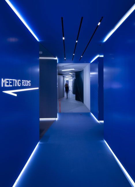 a long hallway with blue walls and lights on the ceiling, leading to a meeting room