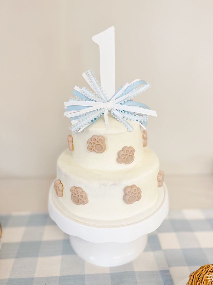 a three tiered cake with blue and white decorations on it sitting on a checkered table cloth