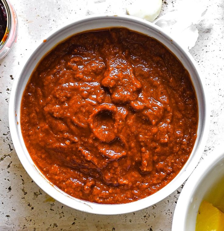 a white bowl filled with red sauce next to two bowls