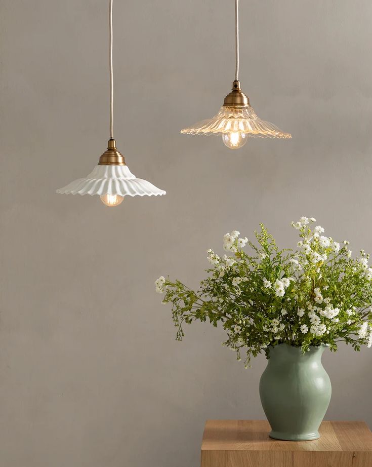 three lights hanging from the ceiling above a vase with flowers in it and one light is on