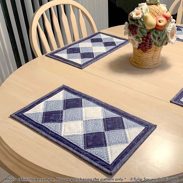 a wooden table topped with two place mats and a vase filled with flowers on top of it