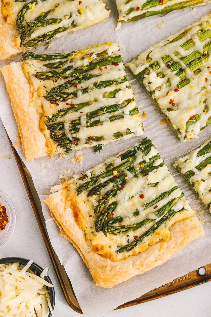 asparagus and cheese pizza cut into squares on parchment paper with serving utensils