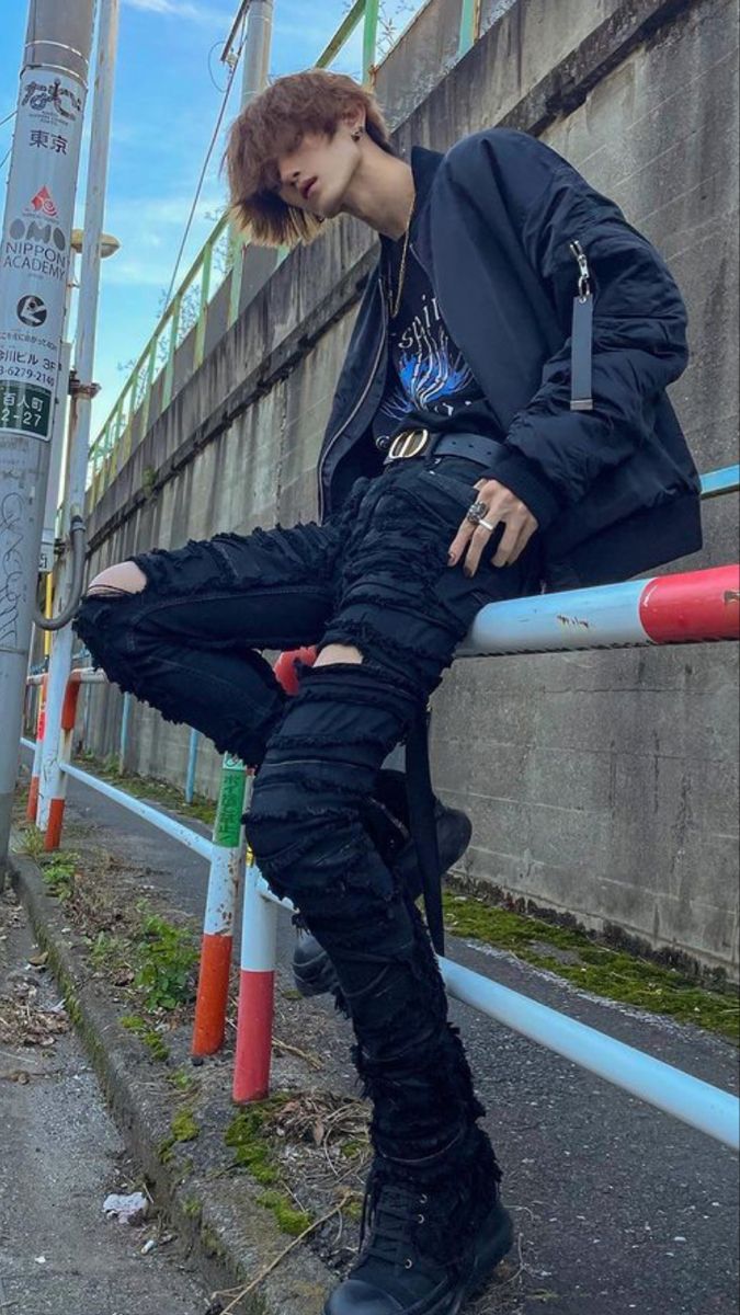 a young man sitting on the side of a road next to a street sign and fence