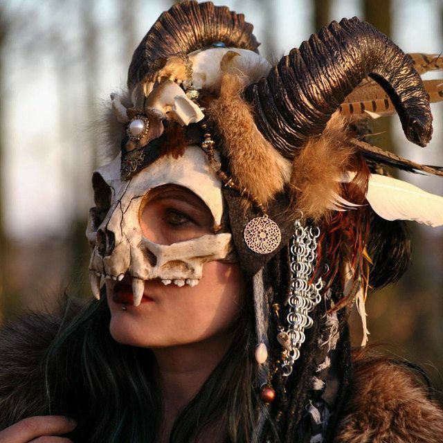 a woman with horns and feathers on her head wearing a mask that looks like an animal's skull