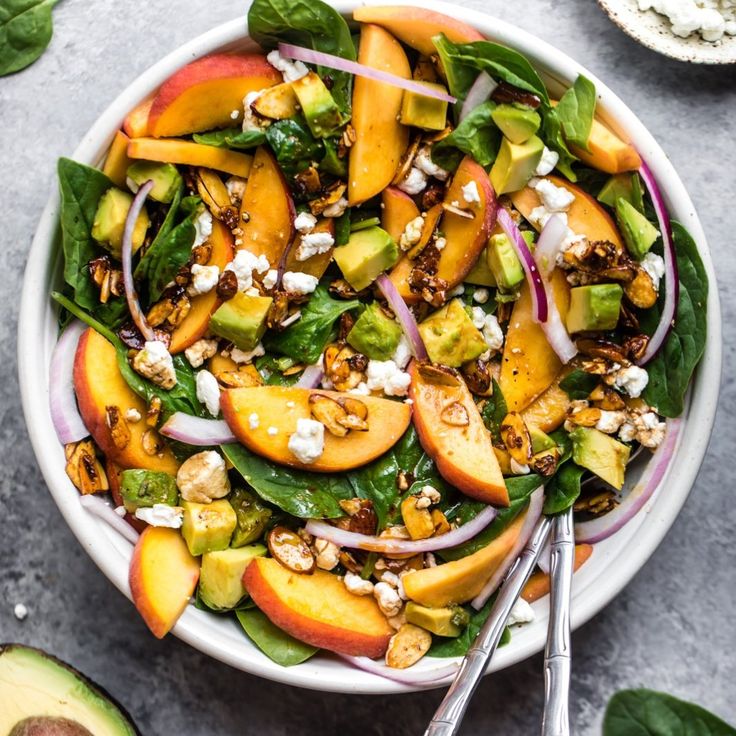 a salad with peaches, spinach and feta cheese in a white bowl